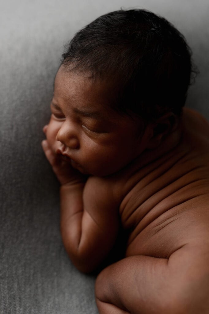 Stunning maternity portrait of a woman dressed elegantly in a black long-sleeve dress posing in front of a dark grey backdrop
