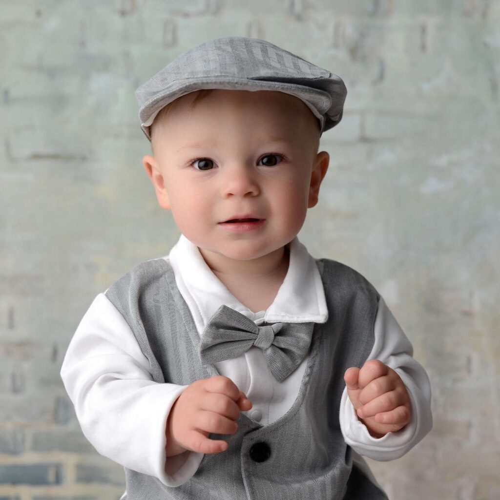 Newborn portrait of a baby in a gray vest and bow tie with a soft smile