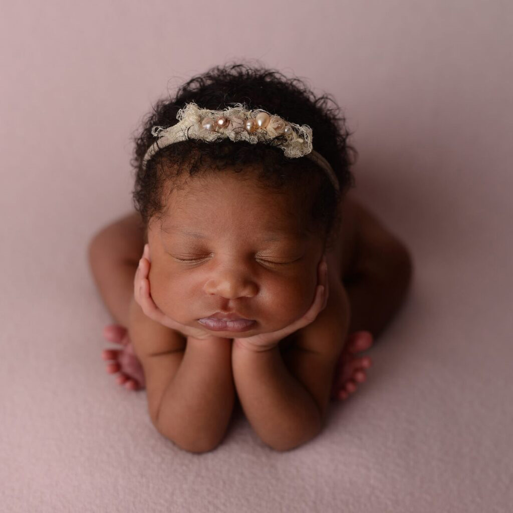 Newborn portrait of a baby girl with a headband posing on a pink blanket