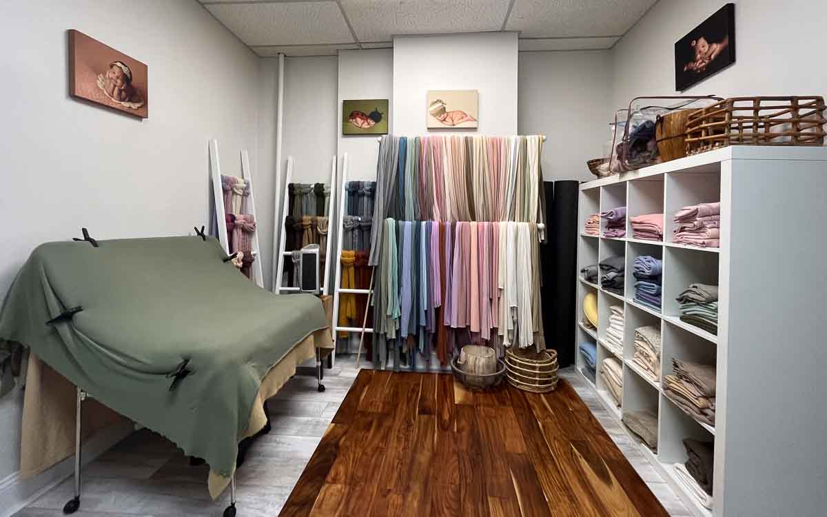 A photo of a studio room containing all sorts of fabric options to choose from and a table for staging newborn portraits.