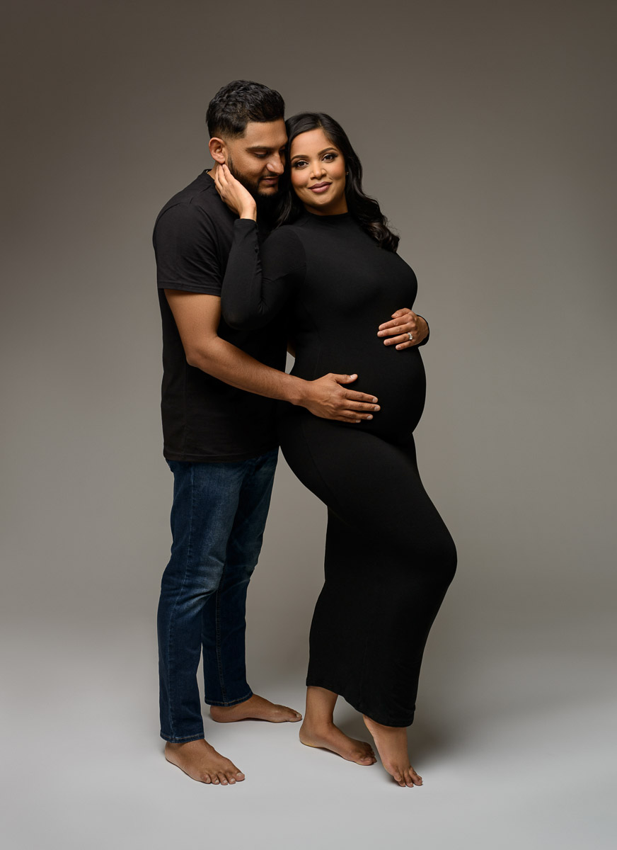 Professional maternity portrait of a couple. The man holds the expecting mother while the mother looks at the camera and smiles.