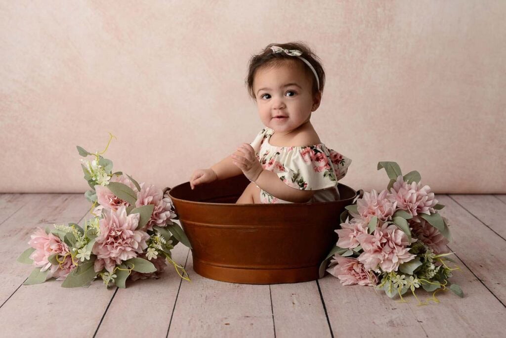 Artistic baby portrait of little girl sitting in a bucket surrounded by pink flowers