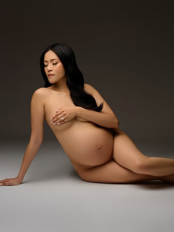 Pregnant woman posing artistically on studio floor.