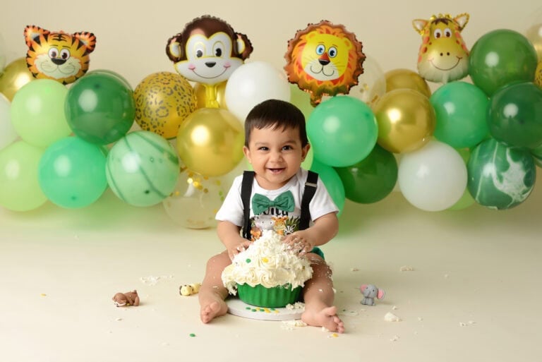 Baby enjoying birthday cake with animal balloons.